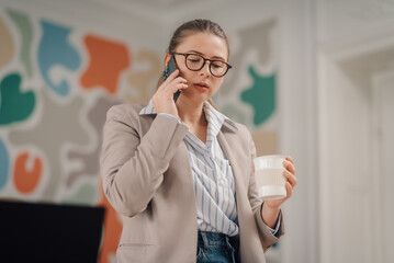 Businesswoman talking on phone and holding coffee in modern office