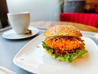 Delicious chicken burger with fresh lettuce and tomato on a white plate with coffee