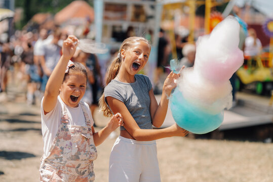 Two cheerful girls holding cotton candy at amusement park - Powered by Adobe