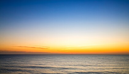 A serene seascape captures the transition from a vibrant orange horizon to a clear blue sky at sunset, reflecting light on the calm ocean surface.