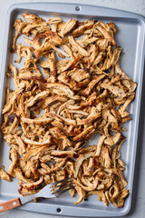 Close-up of shredded chicken in tray and fork on white background.