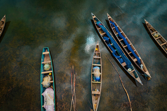 Aerial view of canoes floating on the water, their nets casting sapphire shadows on the shimmering riverbed, creating a mesmerizing dance of light and reflection, Location data omitted.