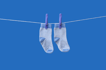 Pair of baby socks hanging on rope against blue background