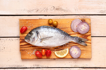 Board of raw dorado fish with lemon and vegetables on light wooden background