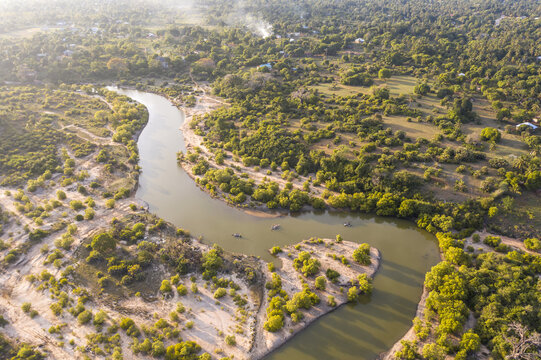 Aerial view of Kongo river cutting through a verdant landscape dotted with trees and foliage, reflecting the sky's soft light, Tiwi, Kwale County, Kenya.