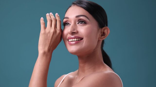 A gorgeous woman strokes her shoulder while turning her body, flashing a wide, radiant smile full of confidence and charm.