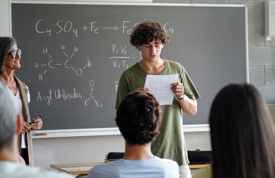 College student presenting a science assignment reading a presentation to classmates and teacher at High School classroom