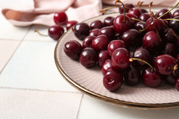 Plate with sweet cherries on white tile table