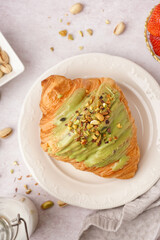 Plate with sweet croissant and pistachio nuts on white background