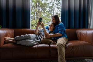 Happy lesbian couple relaxing on couch taking selfie together at home