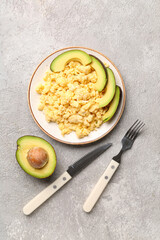 Plate of tasty scrambled eggs with avocado on grey background