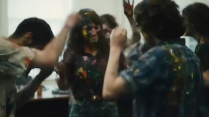 A group of happy young friends, covered in colorful paint, dance and laugh together at a messy and fun indoor party