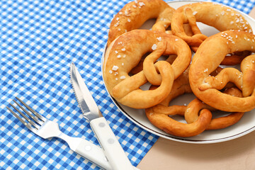 Plate with soft pretzels and cutlery on beige background