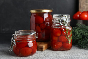 Jars of pickled tomatoes with rosemary and dill on grey table