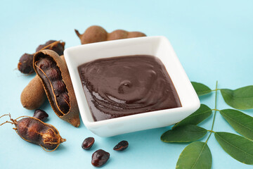 Bowl with tasty tamarind jam and fruits on blue background