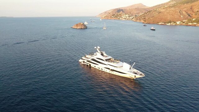 Idra, Greece - 30 July 2025: Aerial view of a luxurious white yacht sailing in the blue waters of Idra bay, with an island and hills nearby.