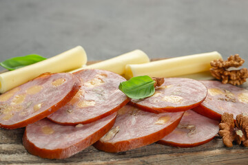 Sliced sausage with cheese, walnuts, and basil served with cheese sticks on wooden board. copy space