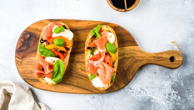 Two open-faced bruschetta topped with prosciutto, mozzarella, tomatoes, and basil, displayed artfully on a wooden cutting board. - Powered by Adobe