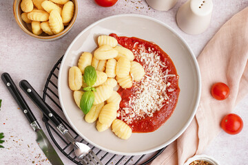 Plate and bowl of tasty gnocchi with tomato sauce and cheese on white background