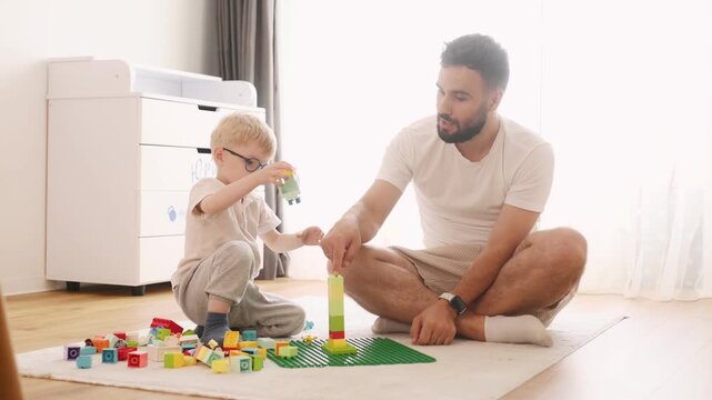 Father is playing in the room with his little son with construction sets.