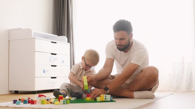 Having a great weekend. Father is playing in the room with his little son with construction sets.