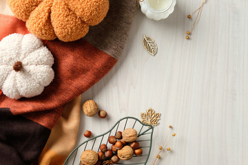 Plush pumpkins with candle, leaves, and basket of nuts on cozy autumn textile. Warm harvest flatlay ideal for seasonal decor and Thanksgiving visuals.
