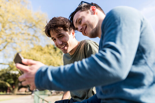 Smiling men sharing smart phone at park