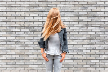 Woman with hair in front of face standing against gray brick wall