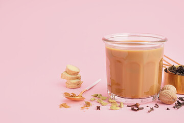 Glass of tasty masala tea with different spices on pink background
