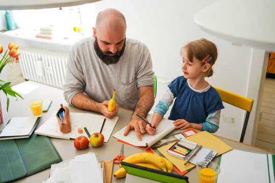 Father helping daughter doing homework sitting at table in home