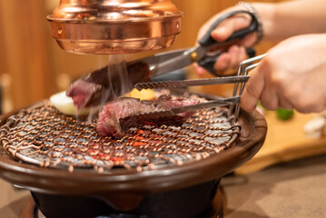 Close-up of hands grilling meat on a Korean BBQ grill with tongs