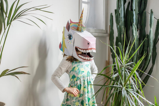 Girl with unicorn mask standing in front of white wall at home