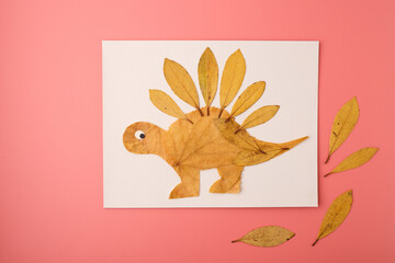 dinosaur stegosaurus made of yellow leaves on paper, eco diy project for children education, suitable for school lessons, publishing, creative workshops, learning platforms and eco friendly campaigns, © Elena