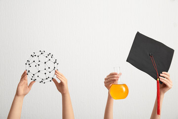 Female hands holding graduation hat with filled flask and molecular model on white background. Chemistry lesson concept
