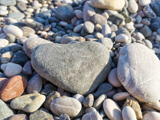 Heart-shaped stone rests prominently among a variety of smooth pebbles on a sunlit beach, showcasing the beauty of nature and the tranquility of the coastal environment