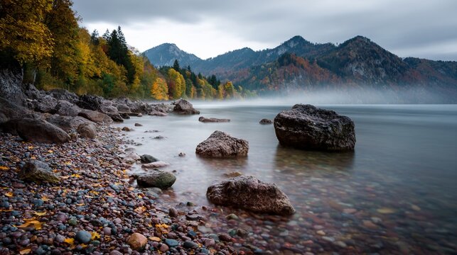 Autumn shoreline with colorful trees, rocks, misty water, and mountains - Powered by Adobe