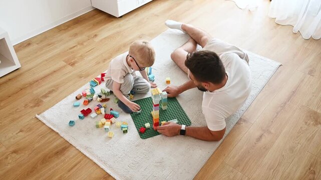 Father is playing in the room with his little son with construction sets.