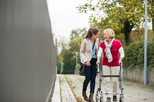 Adult granddaughter assisting her grandmother walking with wheeled walker