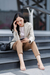 Stressed businesswoman reading bad news on smartphone while sitting on stairs outside office