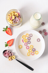 Bowl of colorful sweet cereal rings with milk and cut strawberry on white background