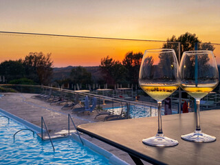 Obraz premium White wine glasses resting near poolside, capturing golden sunset light reflecting on serene Tuscan landscape