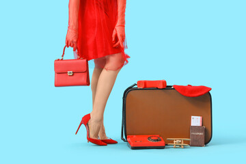 Female traveler with suitcase, retro telephone and beach accessories on blue background