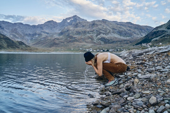 Woman washing face at lakeshore, Splugen Pass, Sondrio, Italy