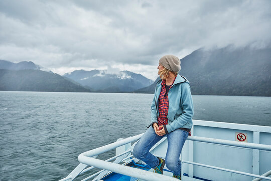 Chile, Hornopiren, woman sitting on rail of a ferry looking at fjord