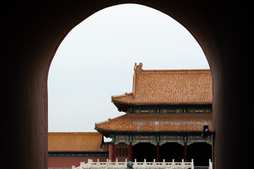 A majestic East Asian imperial palace, viewed through the silhouette of a grand archway. The framing reveals a traditional yellow tiled roof, ornate details, and a white marble bridge.