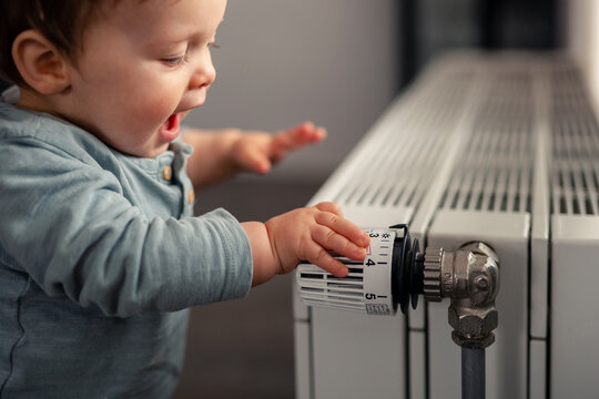Excited baby boy playing with thermostat of heater