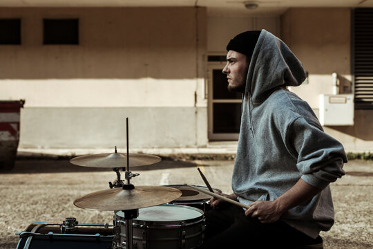 Handsome musician wearing hood playing drums at back yard