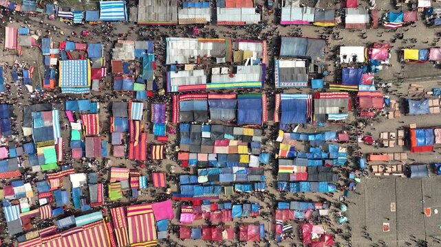 Bogura, Bangladesh - 17 August 2025: Aerial view of a bustling market, alive with vibrant colors from tents contrasting the neutral ground, filled with people.