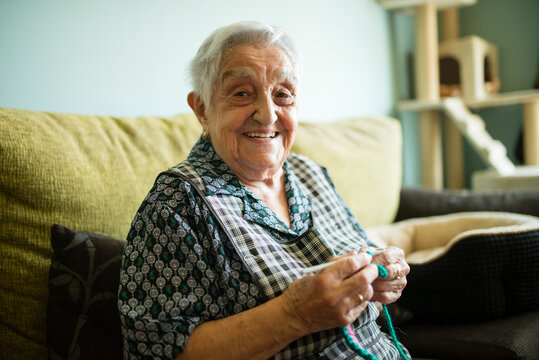 Portrait of smiling senior woman crocheting on the couch at home