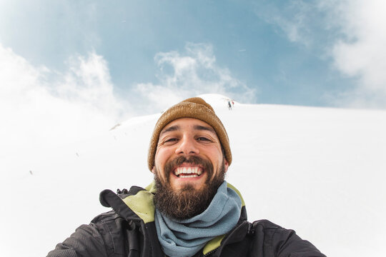 Happy man wearing knit hat taking selfie in snow